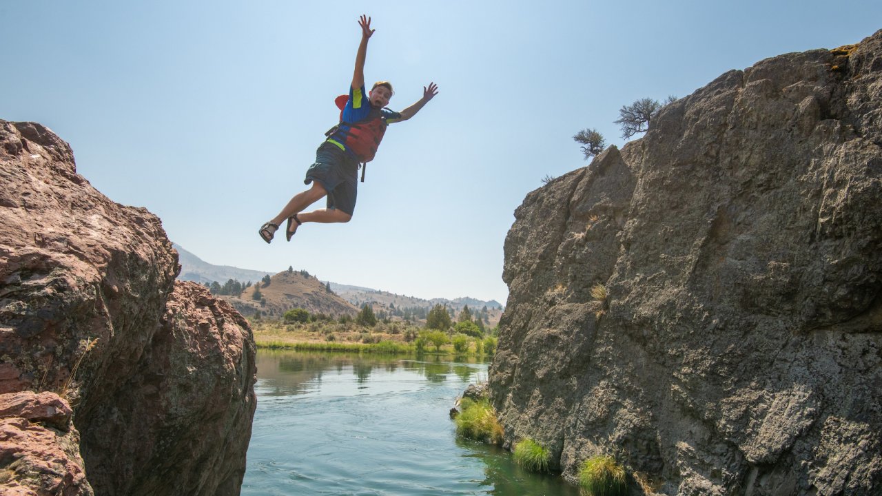 Kid cliff jumping off a basalt boulder into the Deschutes River in Central Oregon