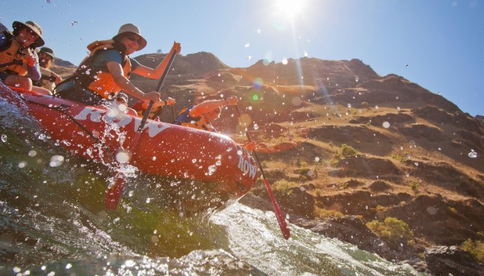 People in a red raft paddling through the Snake River as seen from river level.