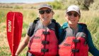 Two guests wearing red life jackets and the one on the left holding a red paddle smiling