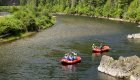 Two red rafts moving down flat water smiling up at the camera 
