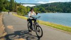 Smiling woman rides an e-bike along a paved trail by Lake Coeur d’Alene in North Idaho, a popular biking destination