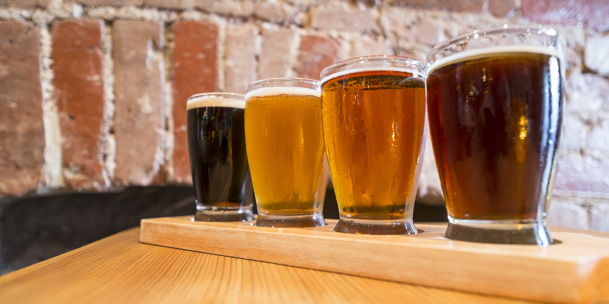 A flight of beers on a wooden table in front of a brick wall