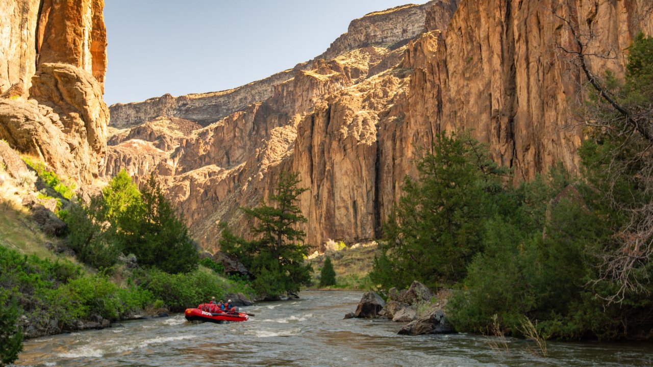 A red raft curving around a river bend between canyon ways on the Bruneau River in Idaho