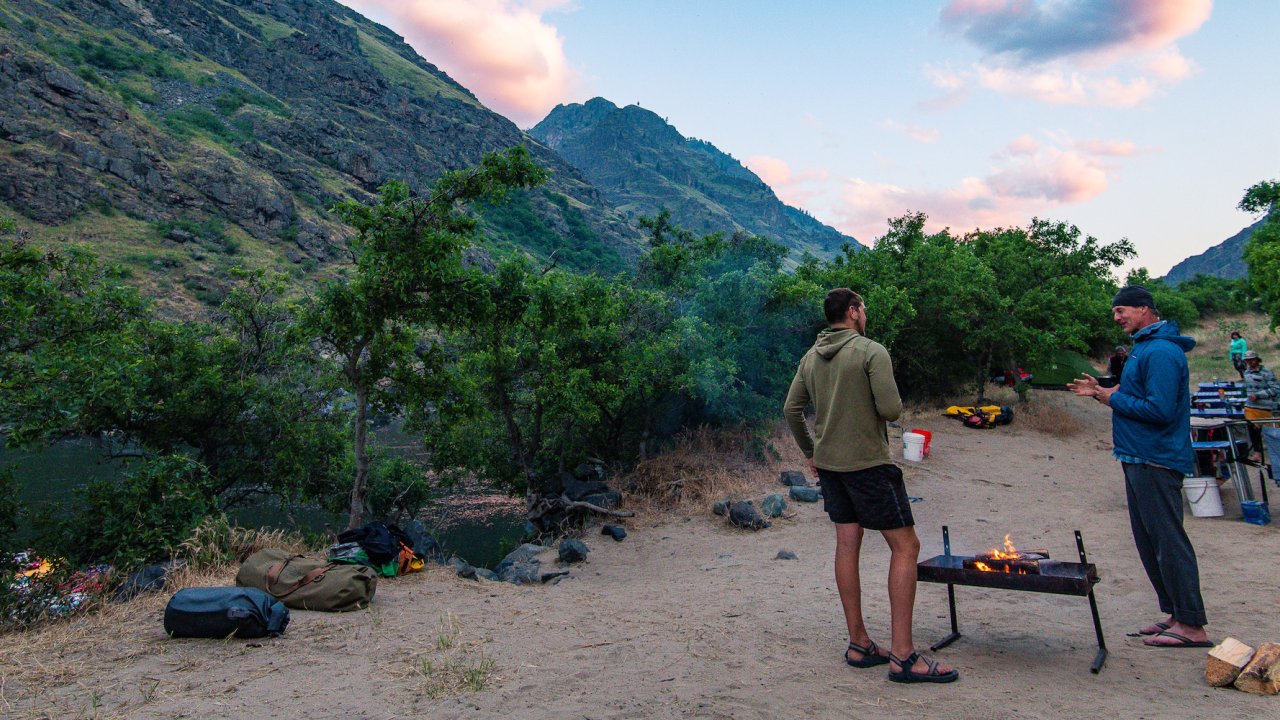 Two men standing around the campfire at dusk along the Snake River in Hells Canyon