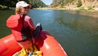 Person relaxing at the front of a red ROW Adventures raft, floating down Idaho’s Clearwater River surrounded by forested canyon walls on a sunny day.