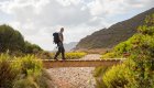 A person walking across a bridge in Corsica with greenery surrounding them. 