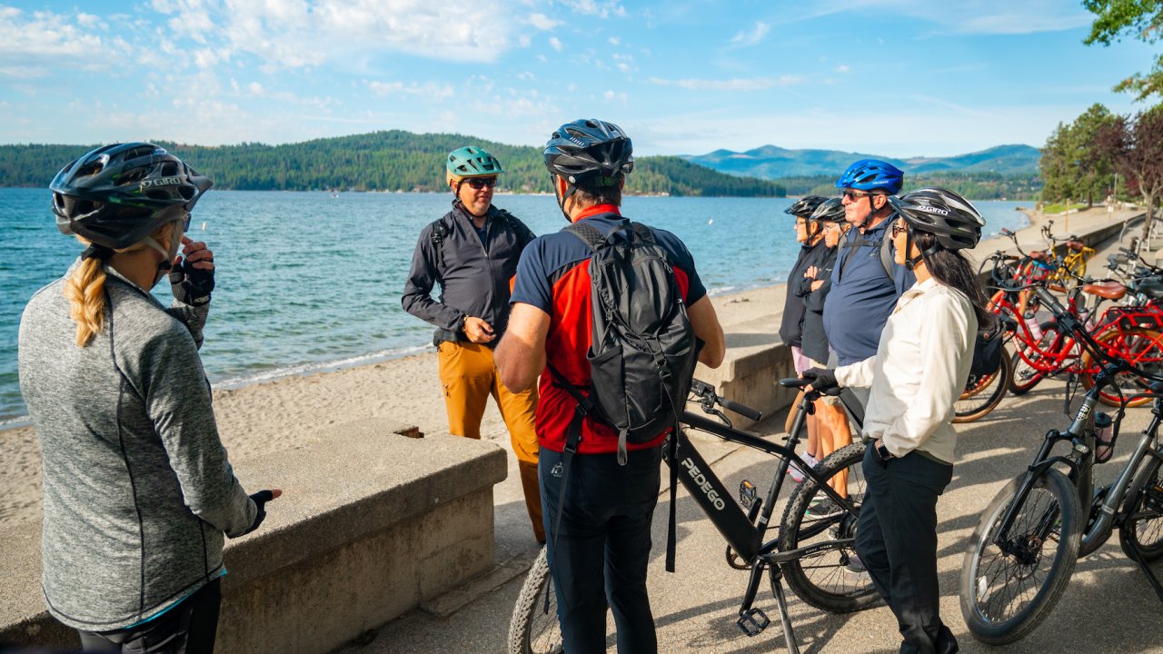 Group of people beside their bikes by a body of water conversing on a sunny day on a chartered e bike tour
