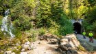 Group of cyclists ride past a waterfall and historic tunnel on the scenic Idaho Hiawatha Bike Trail.
