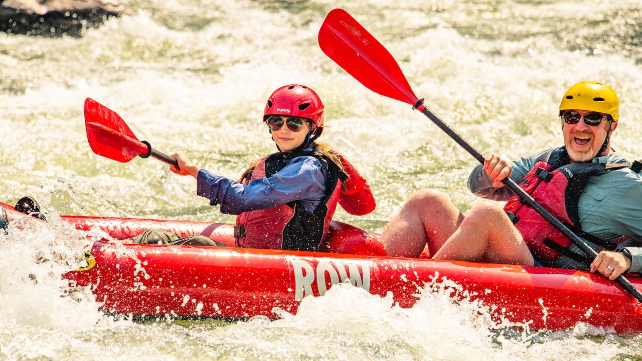 Family rafting vacation with a parent and child paddling an inflatable kayak together through whitewater rapids on a guided river trip