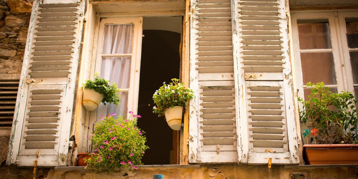 Old white European barn door windows open with flowers and greenery lining the window 