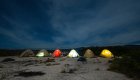 A line of six tents lit up from headlamps beneath a nights sky in the Galapagos Islands