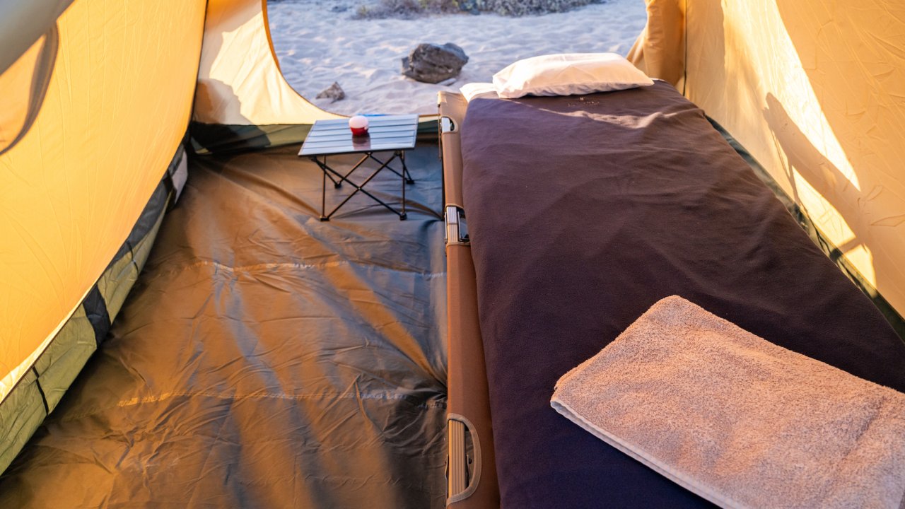 A cot set up inside of a tent with a sleeping bag, pillow, and towel set up for the tent guest