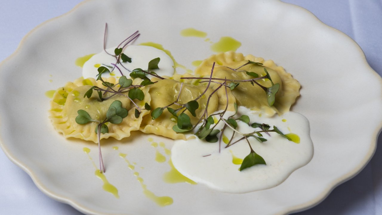 A plate of gourmet ravioli topped with greens, olive oil, and served with a white sauce.