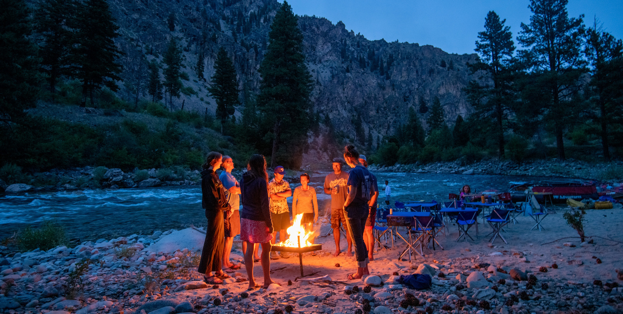 A group of people gathered around the campfire while on a group travel trip along the Middle Fork Salmon River