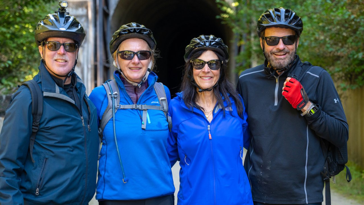 Four people all wearing helmets smiling while on a group bike tour