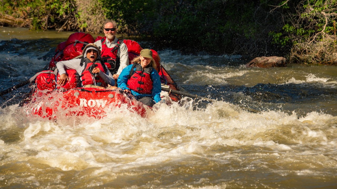 People smiling while being rowed through a whitewater rapid on the Bruneau River in Idaho