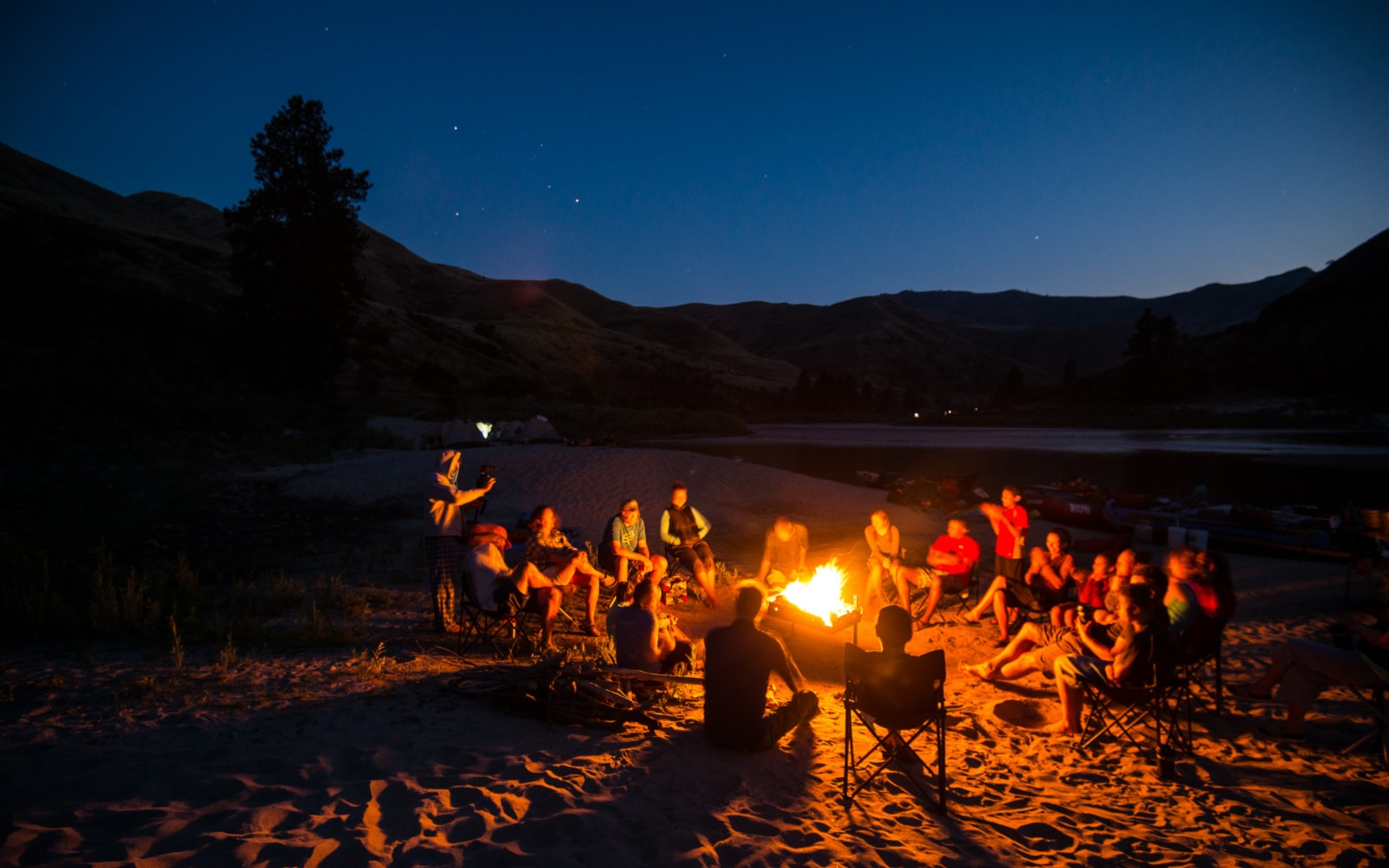 A group of people seated around a campfire on a clear night.