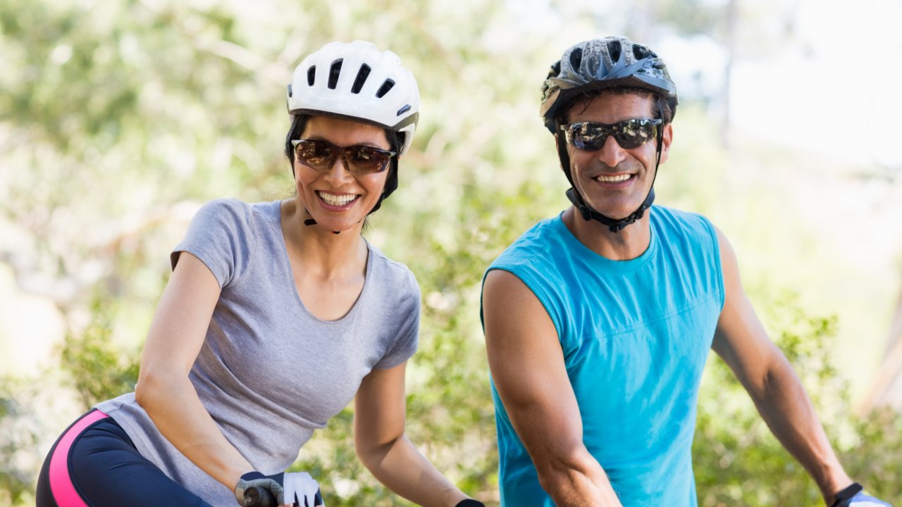 Husband and wife smiling on their bikes with helmets and sunglasses on