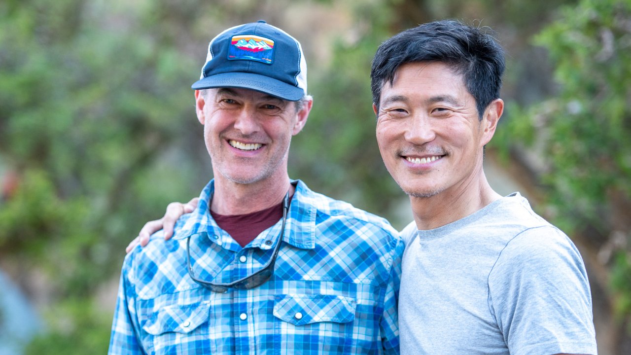 Two men smiling for a photo while camping