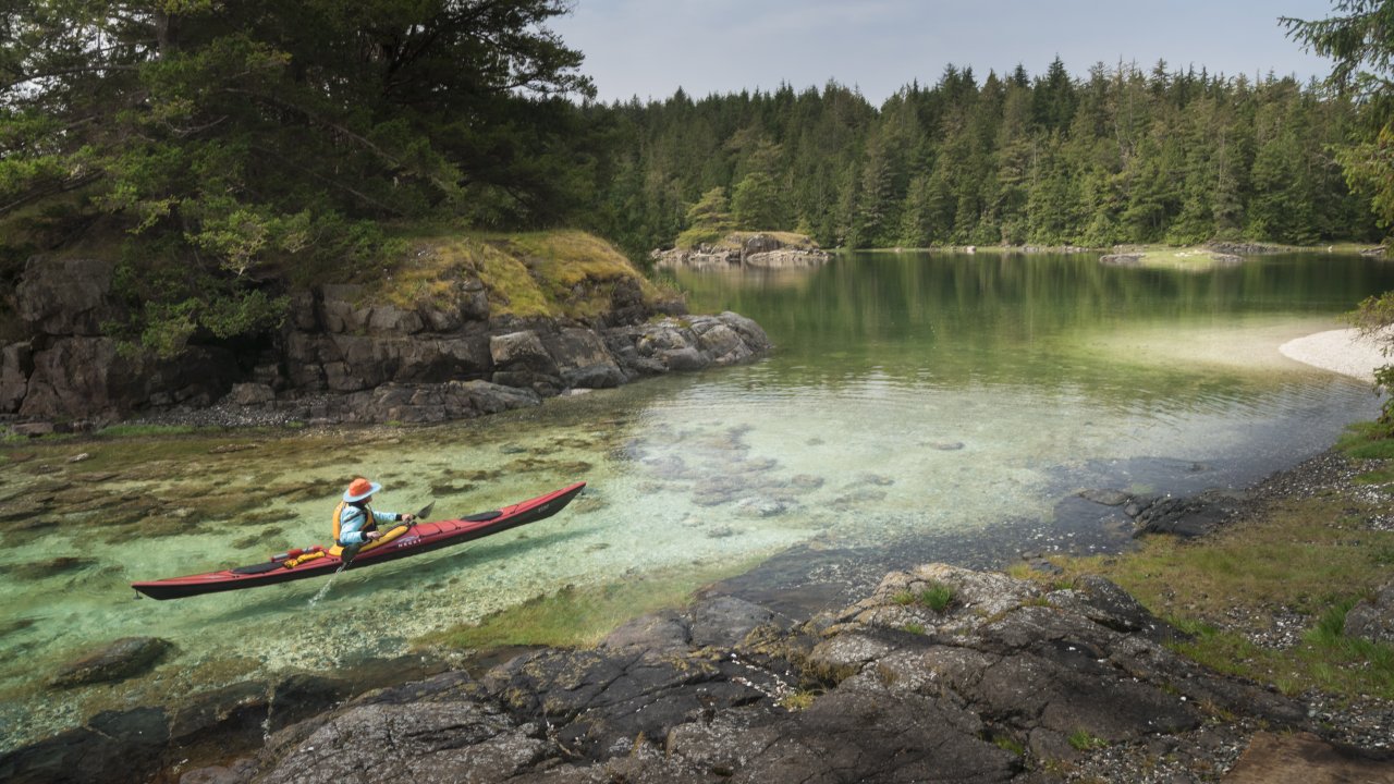Kayaker moving through a narrow channel over crystal clear waters in British Columbia
