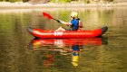 Kayaker paddling a red ROW Adventures inflatable kayak on Idaho’s Clearwater River, reflected on calm water with sandy shoreline in the background — peaceful rafting and kayaking trip.