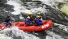 A red raft moving fast on the river with passengers 