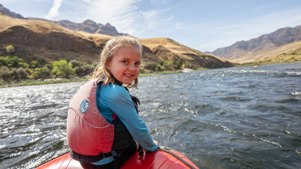 A young girl sitting on the front of a red ROW adventures raft smiling.