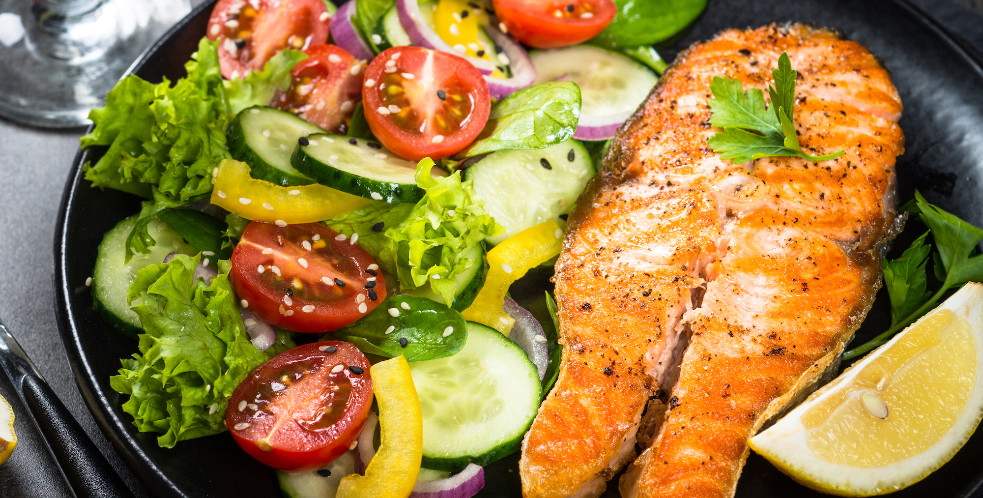 Salmon dinner on a black plate with a fresh salad and a lemon wedge