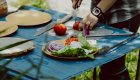 Person cutting a red onion with a lunch spread presented in front of them on a blue table