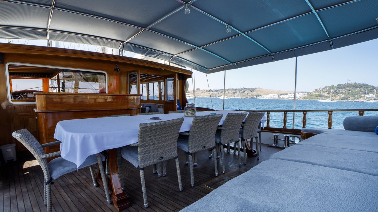 Two long rectangular tables with white table clothes and place settings on a ship deck