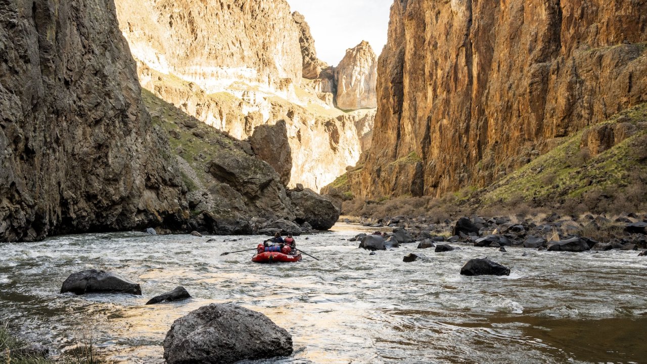 A raft floating down the Owyhee river with scenic cliffs surrounding the river.