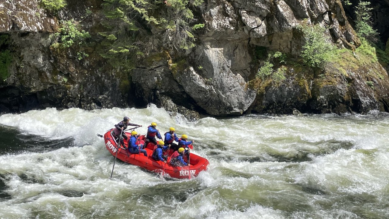 Side view of a red raft in a whitewater rapid with a large rock wall behind it