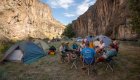 A group of people sitting around a camp table next to a group of tents at sunset
