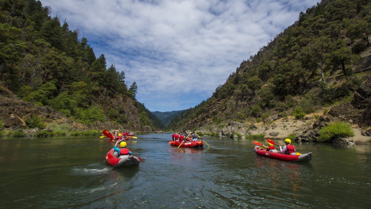 Rafts and inflatable kayaks floating on the Rogue River in Oregon, combining rafting excitement with overnight camping along the riverbanks.