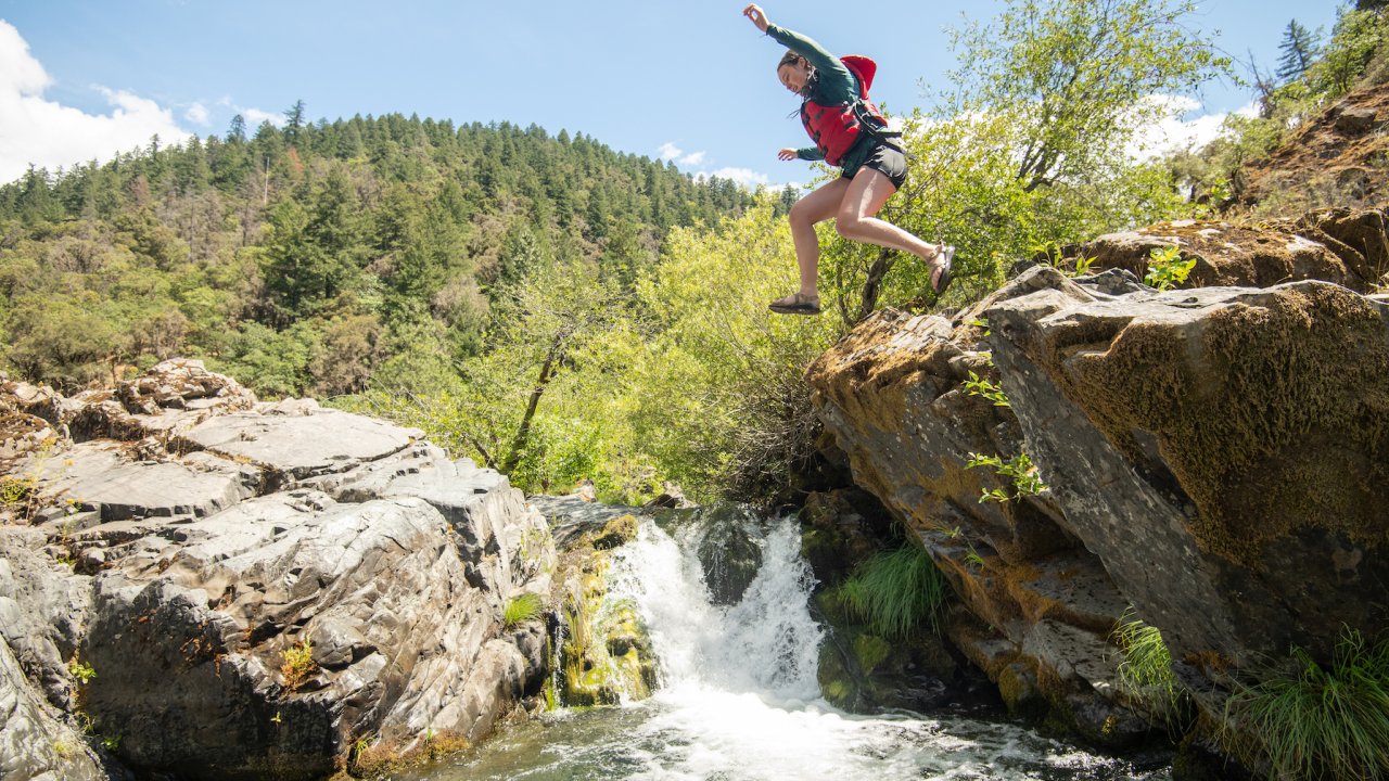 Girl jumping off a rock into a small pool below a waterfall in Oregon