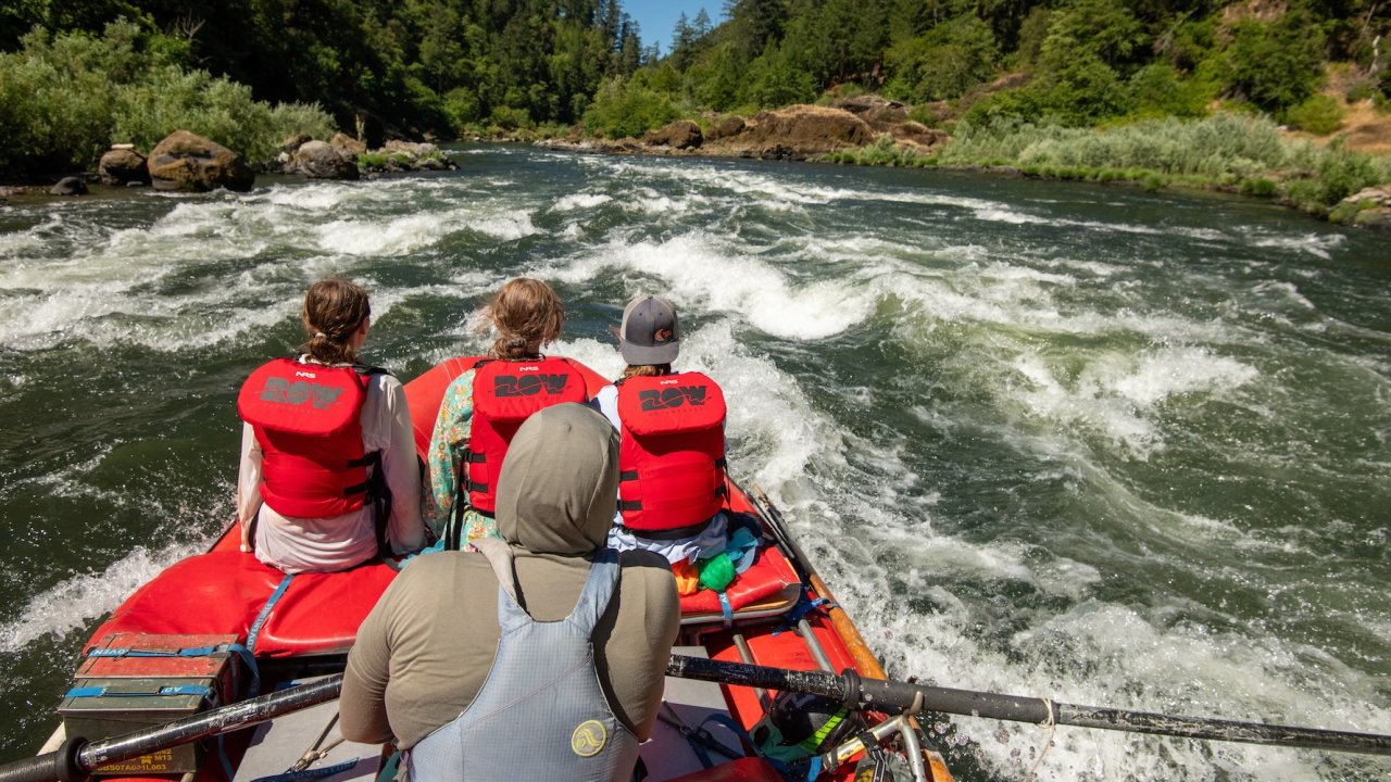 View from the back of a raft as adventurers ride rapids on the Rogue River in Oregon, capturing the beauty and excitement of Oregon rafting vacations.