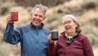 Close up on a man on the left and woman on the right holding up aluminum camping mugs and smiling