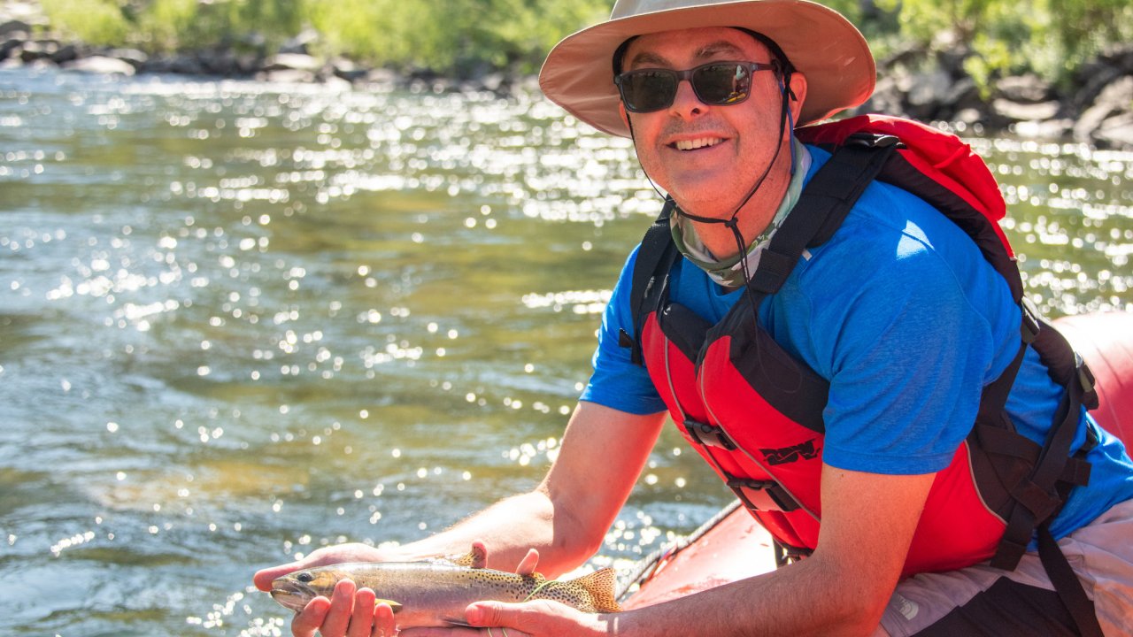 Person leaning over a red rafting holding a fish just out of the Salmon River