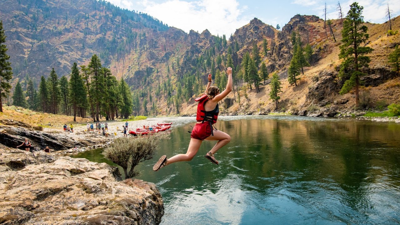 Guest jumping off a riverside cliff into the Middle Fork of the Salmon River in Idaho, enjoying a thrilling moment during a guided rafting and adventure tour.
