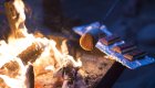 Marshmallow roasting over a campfire with s’mores ingredients nearby.