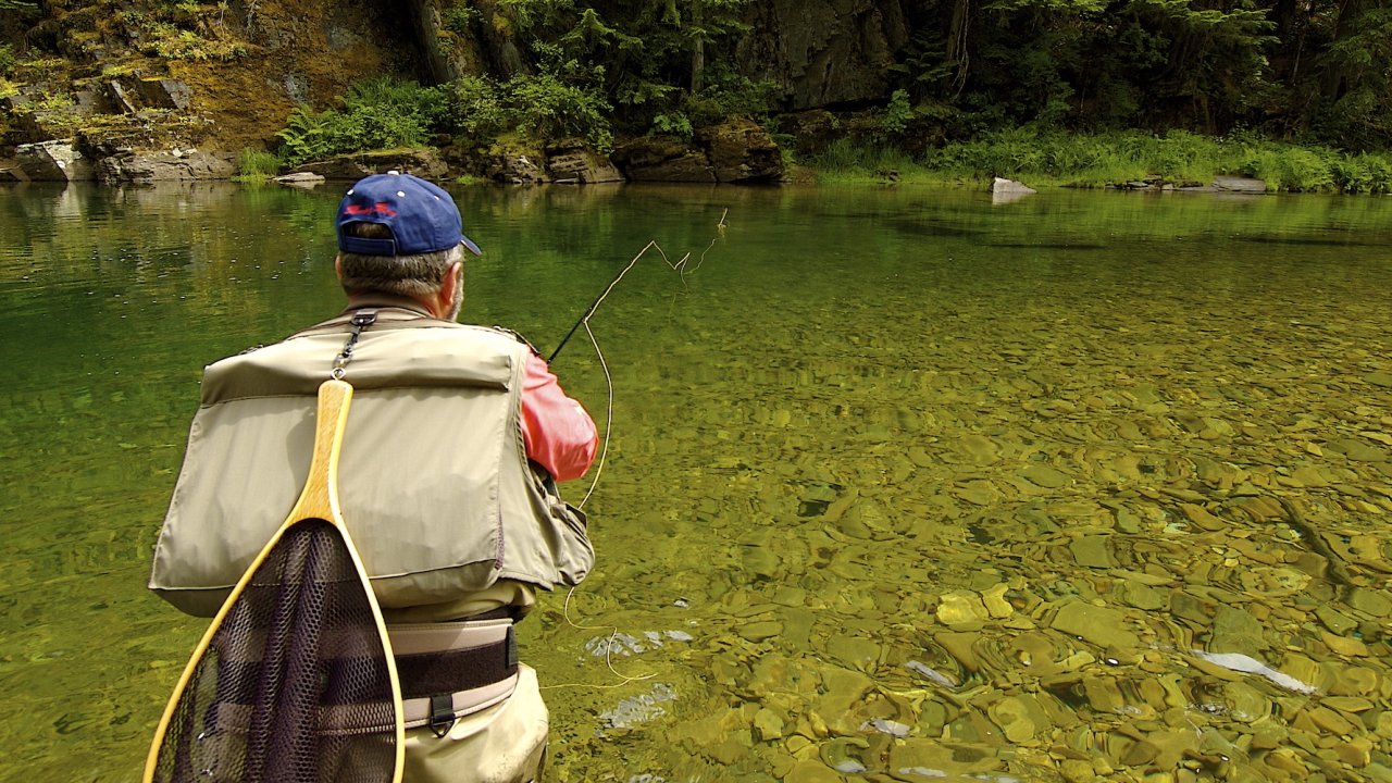 Person casting a yellow line into the St. Joe River in North Idaho with a net behind his back