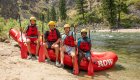 Four kids sitting on a red holding their paddles on a sunny day in Idaho