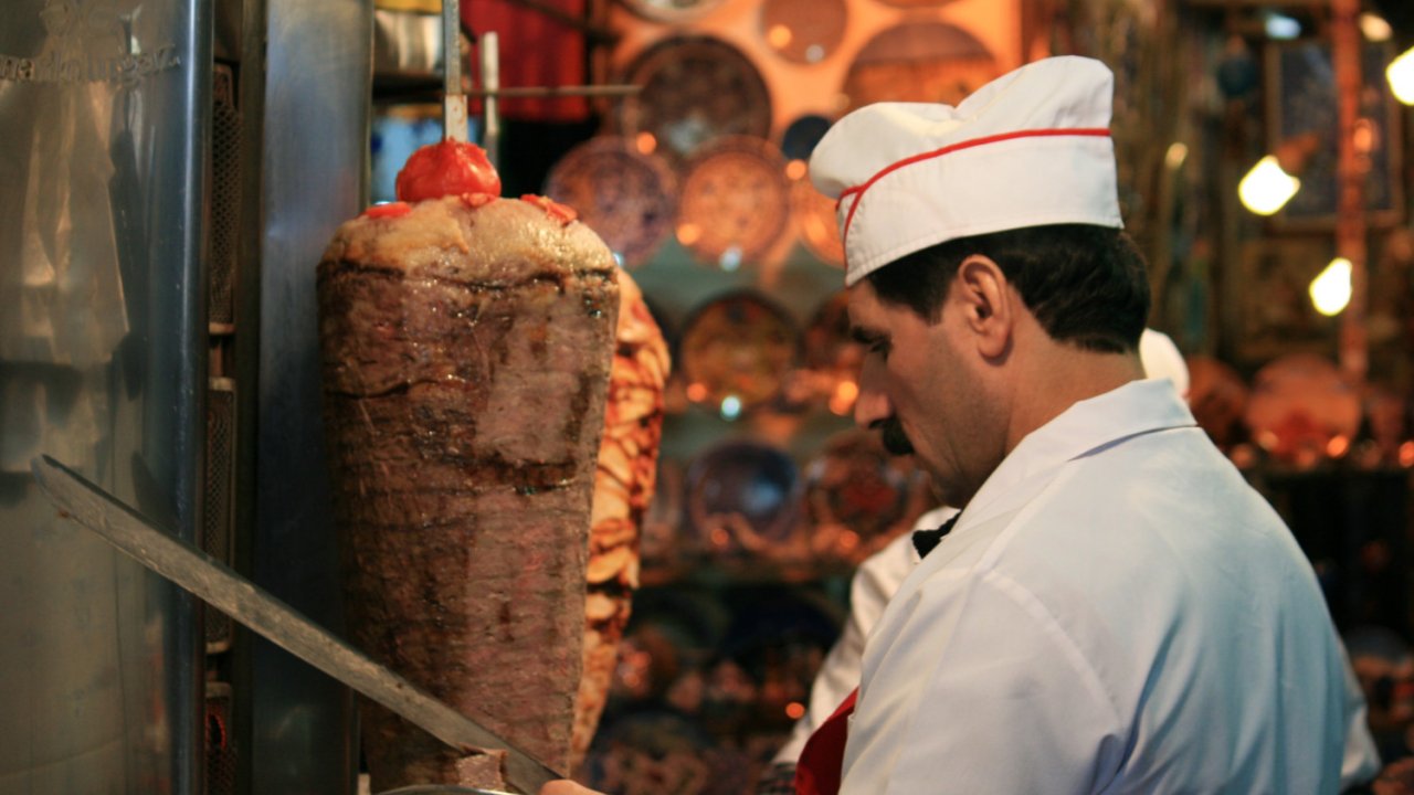 A person in a white chef suit cutting lamb roasting in Turkey