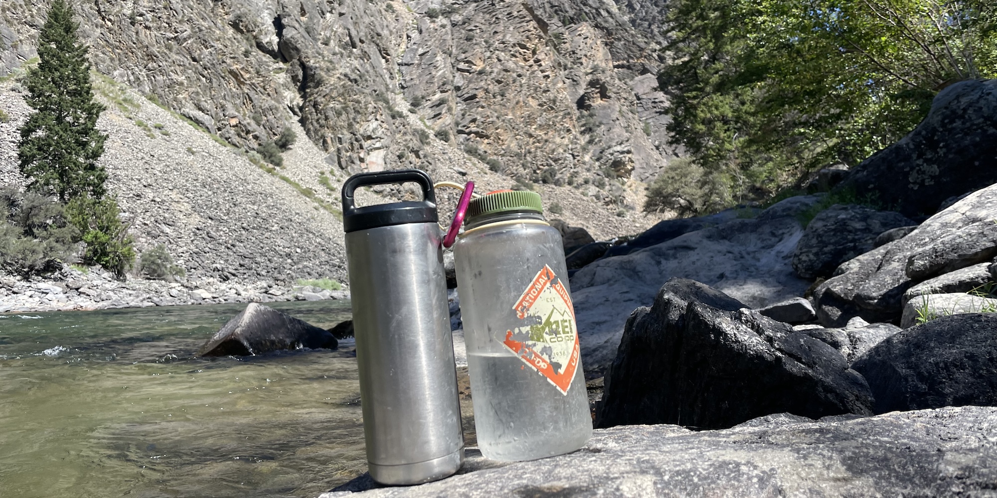 Two water bottles and one carabiner sitting on a rock next to the Salmon river.  