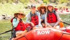 Group of rafters sitting on the front of a red ROW Adventures raft, smiling as they float down Idaho’s Clearwater River with another raft group visible in the background.