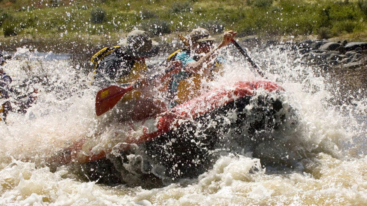 A red ROW Adventures raft crashing through a wave on the Owyhee river in Oregon during a guided rafting tour.
