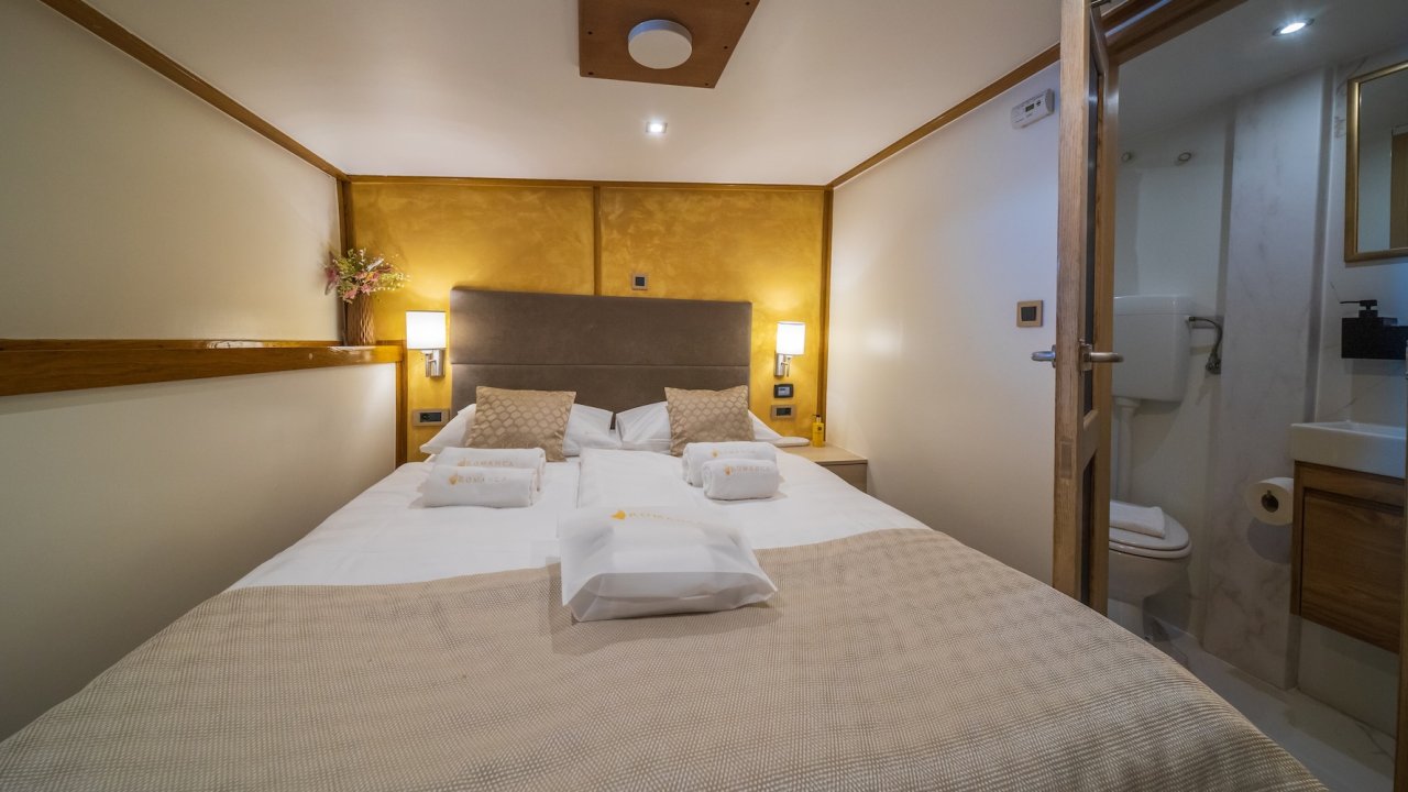 A yacht cabin and bathroom with a made bed.