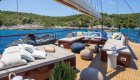 A sun deck on a yacht with cushioned longe seating, a jet ski, and views of the Adriatic Sea and green coastline. 
