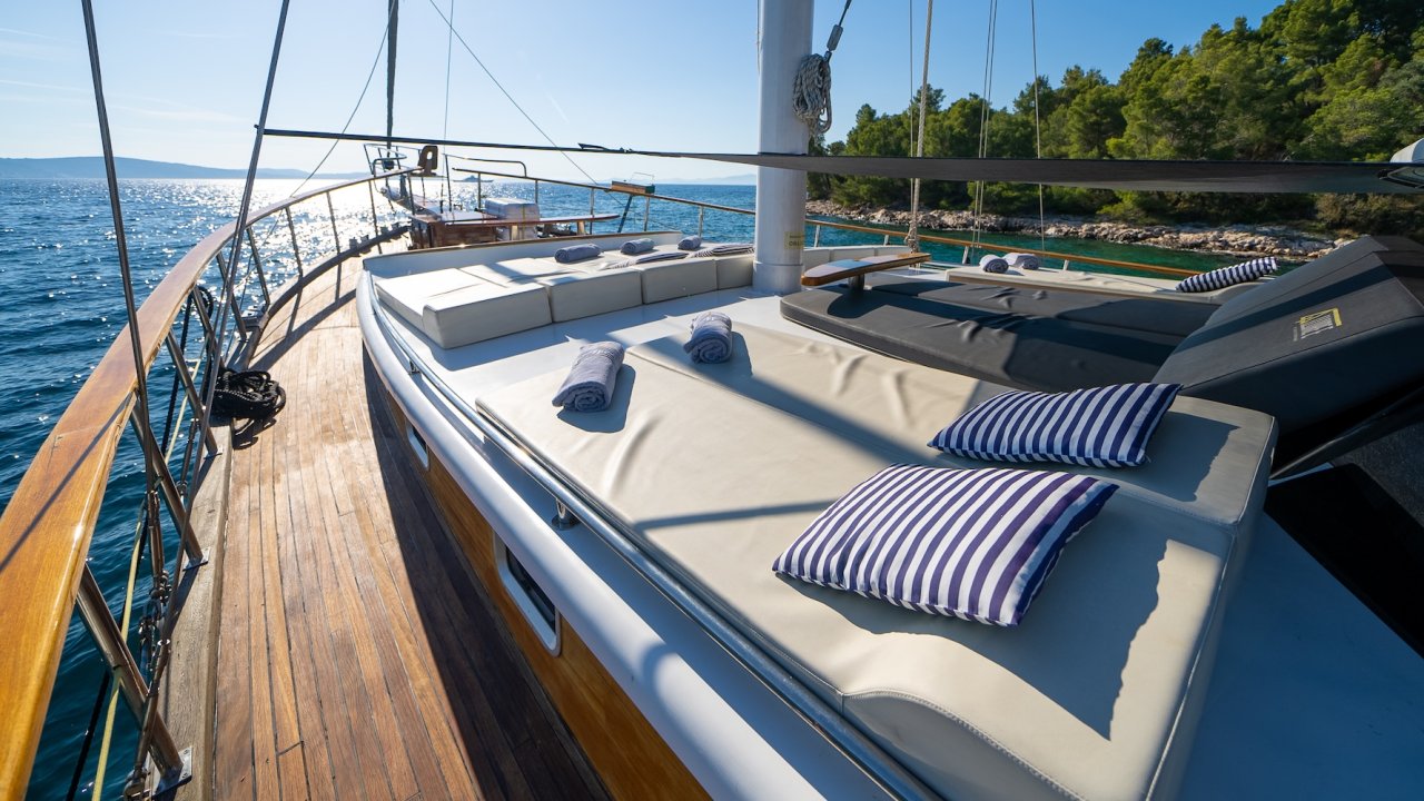 A sun deck on a yacht with cushioned lounge chairs, striped pillows, and ocean views.
